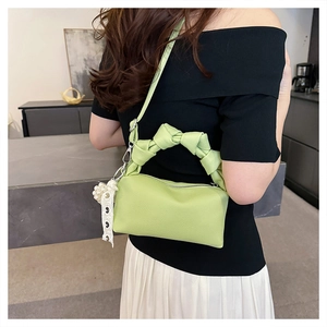 Macro detail of avocado green leather handbag featuring a knotted handle and pearl charm
