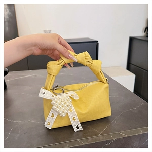Detail of yellow lychee textured mini handbag featuring a knotted strap and pearl heart charm