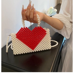Detail of handmade pearl tote bag featuring a red heart pattern and beaded shoulder strap