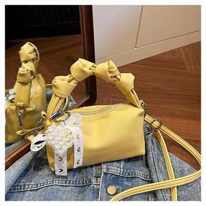 Detail of yellow lychee leather handbag featuring a knotted handle and pearl heart charm