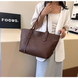 Detail of a large dark brown woven tote bag carried by a model in a minimalist room