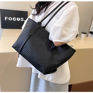 Close-up of a black woven tote bag with a wide shoulder strap and minimal design
