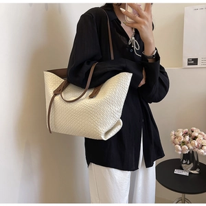 Detail of large beige woven tote bag with brown leather handles worn by a model