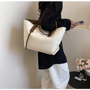 Detail of high-capacity woven tote bag featuring beige leather grid and brown strap