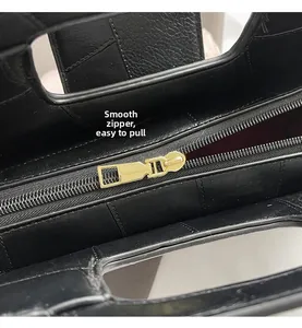 Detail of smooth gold zipper on black lychee grain leather handbag with fine stitching