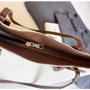 Detail of premium golden zipper and brown leather trim on a white woven tote bag