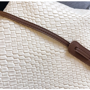 Detail of white woven leather bag texture with dark brown stitched shoulder strap