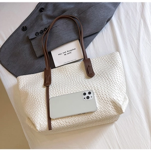 Close-up of white woven tote bag with brown leather handles and smartphone for size scale