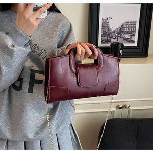 Detail of burgundy PU leather handbag featuring fine stitching and gold chain strap