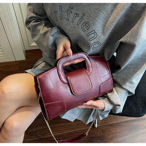 Detail of wine red handbag featuring unique hollow handle and sleek gold chain strap