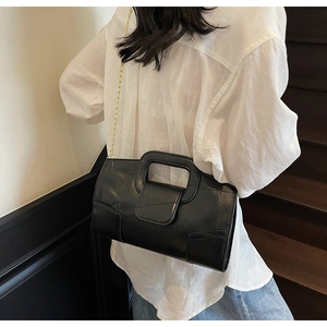 Detail of black crossbody bag with gold chain strap and hollow handle on stairs