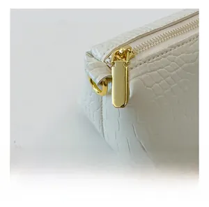 Close-up of golden polished metal zipper on crocodile textured white leather bag detail