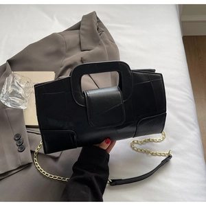 Detail of black geometric leather handbag with gold chain strap on a white bedding background
