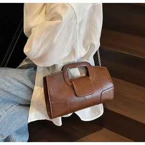 Detail of dark brown leather crossbody bag with chain strap shown on steps