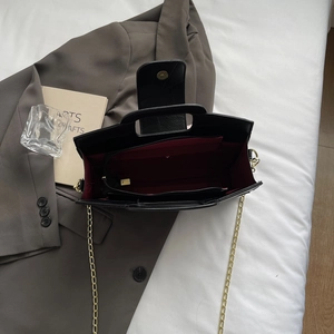 Detailed view of black leather bag with red lining and gold chain strap closure