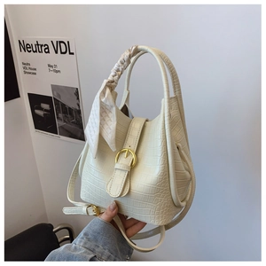 Detail of cream bucket bag with crocodile texture, gold buckle and silk scarf on handle
