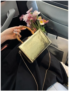 Close-up of golden box bag with bamboo handle and metal chain strap in car interior