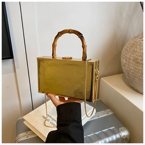Close-up of golden rectangular box bag with bamboo handle and elegant metal chain strap