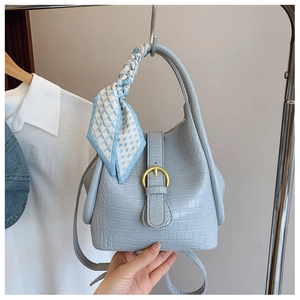 Detail of light blue crocodile texture bucket bag with silk scarf handle and gold buckle