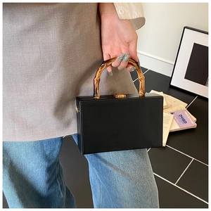 Detail of a black square box bag with an amber bamboo handle and a gold metal lock
