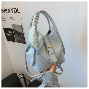 Detail of light blue croc-embossed bucket bag with decorative scarf and gold buckle