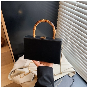 Detail of black box bag with bamboo handle, gold lock and detachable chain strap