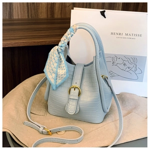 Detail of light blue faux crocodile bag with golden buckle and silk scarf on the handle