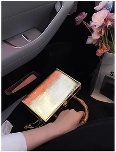 Close-up of golden box bag featuring bamboo handle and vintage metal lock on car seat