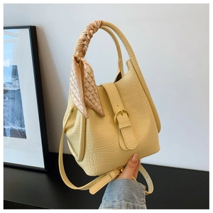 Close-up of yellow crocodile texture handbag featuring a decorative silk scarf on handle