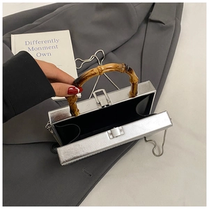 Silver square box bag with bamboo handle and metal chain shown on grey blazer