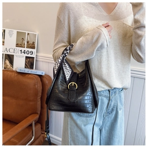 Detail of black crocodile texture handbag with gold buckle and decorative silk scarf wrap