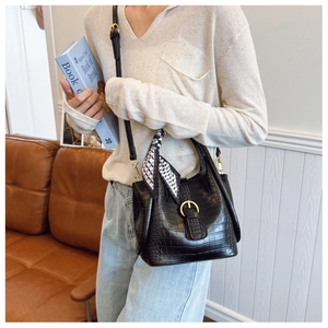 Detail of black crocodile texture bucket bag with gold buckle and decorative scarf