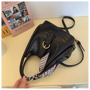 Top view of black croc-effect bucket bag with gold buckle and silk scarf on handle