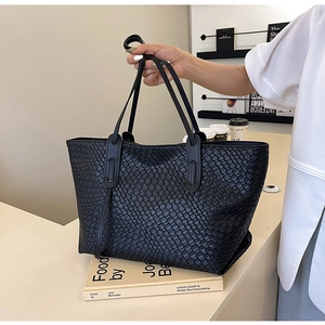 Large black woven tote bag with shoulder straps for women, shown in a stylish lifestyle setting