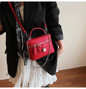 Close-up of red lychee leather box bag with silver chain and metal padlock detail