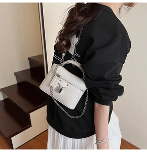 Detail view of a white box-shaped crossbody bag with litchi texture and silver chain
