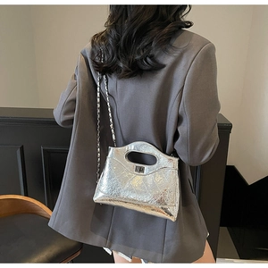 Detail of silver metallic quilted bag with chain strap worn with a grey blazer
