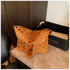 Close-up of orange leather shoulder bag with silver rivet studs on marble tabletop