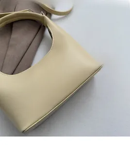 Nahaufnahme einer beigen Tasche mit weicher Leder-Litschi-Struktur und Halbmondform
