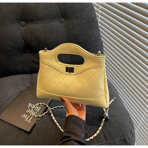 Close-up of beige quilted handbag featuring metal twist lock and chain shoulder strap