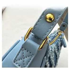 Detail of light blue crossbody bag featuring denim stitching and golden hardware