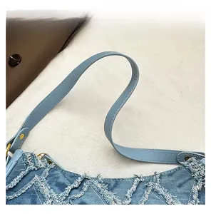 Detail of light blue denim bag featuring frayed edges and smooth leather shoulder strap