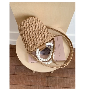 Close-up of beige woven straw bucket bag with white bead handles and brown leather accent