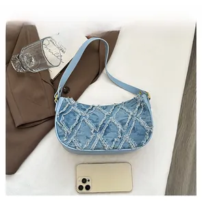 Detail of light blue denim crescent bag with frayed rhombus texture and metal buckle