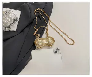 Peanut-shaped gold mini bag with rhinestones shown next to a phone for scale