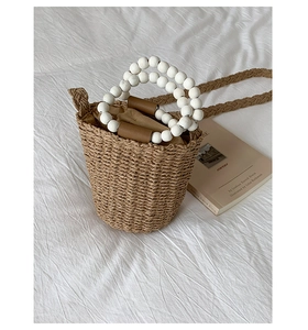 Detail of straw bucket bag featuring white beaded handles and brown drawstring lining