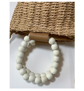 Detail of hand-woven straw bag featuring decorative white wooden bead handles and leather trim