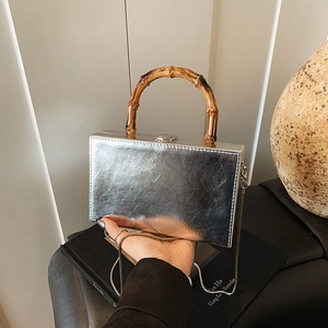 Silver mirror crossbody bag with bamboo handle and metal chain shown in a hand-held view