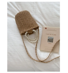 Detail of woven straw bucket bag featuring white beaded handle and elegant fabric lining