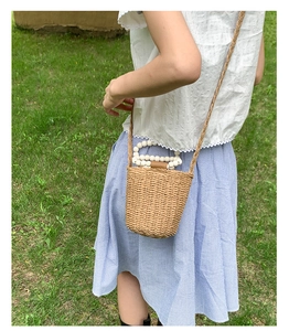 Detail of straw woven bucket bag featuring pearl bead handles and brown leather clasp